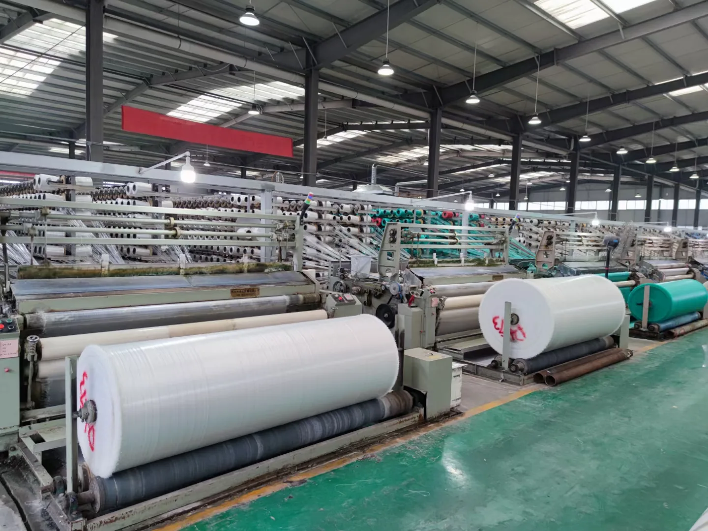 Circular and flat looms weaving high-strength PE woven fabric rolls in a production workshop