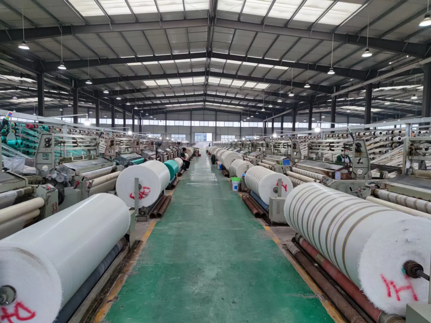 Woven fabric roll production workshop with multiple weaving machines and finished rolls